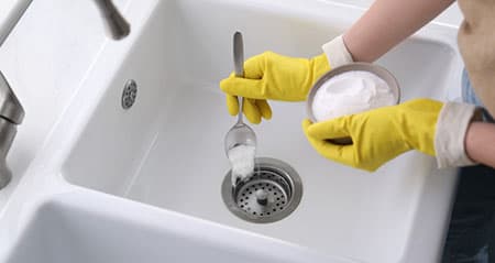 Rohr frei mit Natron: Eine Frau lässt Natron in den Ausguss rieseln