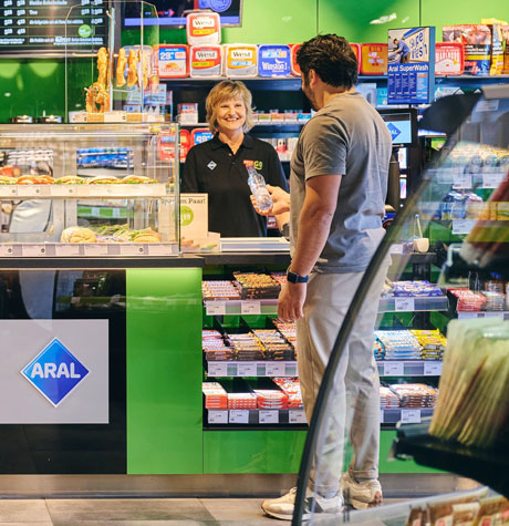 Aral Kasse mit Kunden und Kassiererin hinter dem Tresen