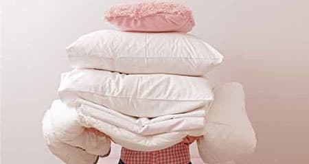 Eine Frau hat Daunendecken und Daunenkissen auf dem Arm.