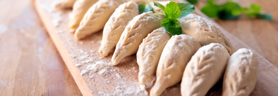 Ungekochte Culurgiones liegen vorbereitet auf einem Holzbrett.