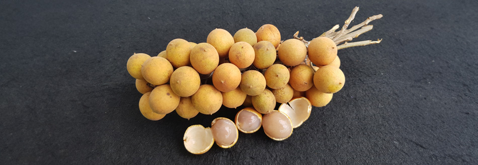 Unversehrte und einige aufgepellte Pitombas liegen auf einer Steinoberfläche.