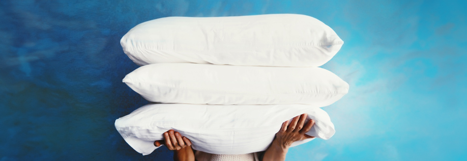 Kopfkissen waschen: Jemand hält drei strahlend weiße Kissen gestapelt auf dem Arm