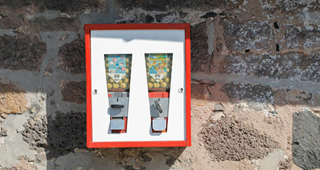 Ein Kaugummiautomat hängt an einer Hauswand und wartet auf Kau(f)willige