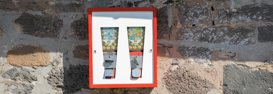 Ein Kaugummiautomat hängt an einer Hauswand und wartet auf Kau(f)willige