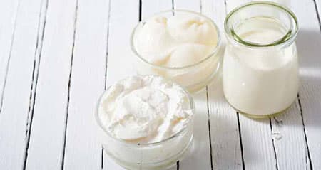 Schmand, Crème fraîche und saure Sahne stehen nebeneinander auf Holz