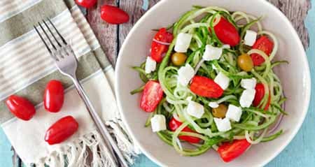Ein Teller mit Zucchini-Nudeln, Tomaten und Mozzarella steht auf einem Tisch