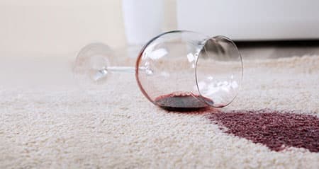 Rotweinflecken mit Weißwein entfernen: Ein umgefallenes Glas mit Rotwein auf einem Teppich