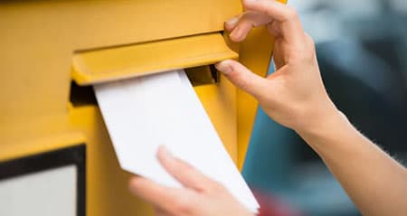 Was kostet ein Brief? Eine Frau wirft einen Umschlag in den Briefkasten