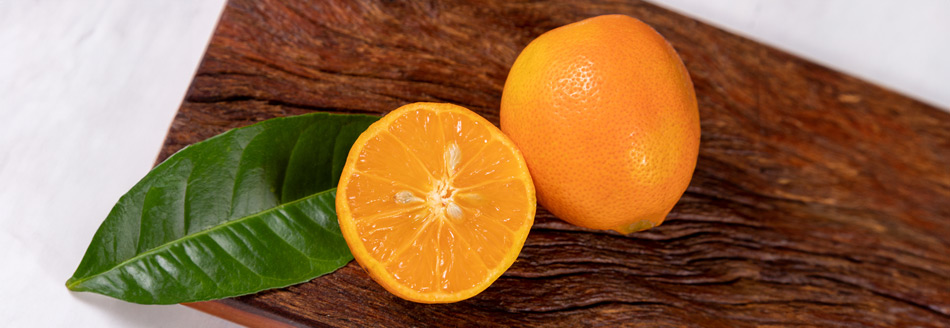 Eine orangefarbene Rangpur liegt neben einer halben Frucht der gleichen Art auf einem dunklen Holzbrett.