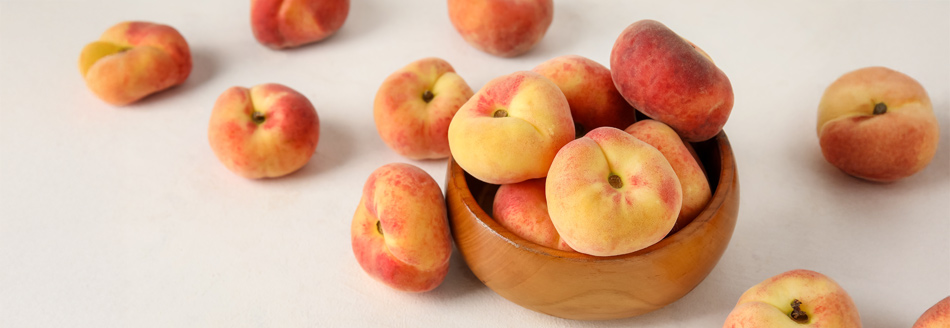 Einige Plattpfirsiche warten in einer Holzschale auf ihren Verzehr