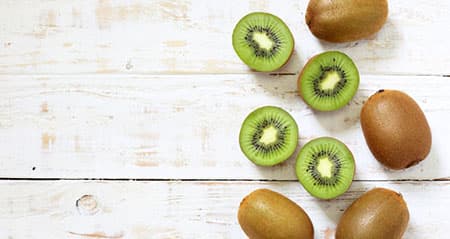 Kiwi mit Schale essen: Ganze und halbe Kiwis liegen auf Holz