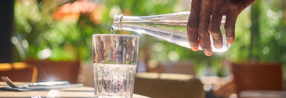 Jemand gießt in einem Restaurant Mineralwasser aus der Flasche ins Glas