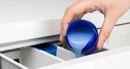 Weichspüler: Jemand füllt Weichspüler in die Waschmaschine