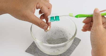 Schmuck reinigen mit Backpulver: Eine Frau putzt Schmuck mit einer Zahnbürste