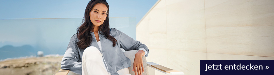 Frau mit dunklen Haaren im heine Outfit sitzt auf einem Stuhl. Jetzt entdecken.