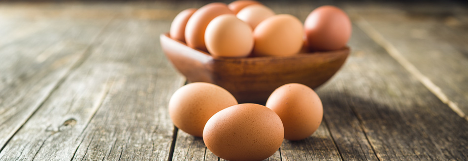 Wie gesund sind Eier? Einige Eier mit brauner Schale liegen auf einer Holzfläche und in einer Holzschüssel