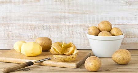 Darf man Kartoffelschalen essen? Kartoffeln liegen z. T. geschält auf einem Holzbrett