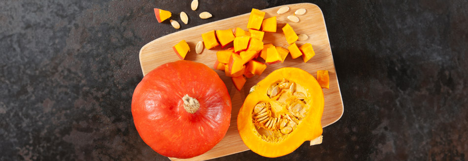 Ein aufgeschnittener Hokkaido-Kürbis liegt auf einem Holzbrett.