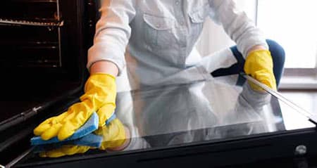 Backofen putzen: Eine Frau putzt die Scheibe des Ofens