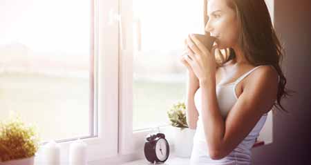 10 Tipps für Morgenmuffel: Eine Frau trinkt Kaffee am Fenster