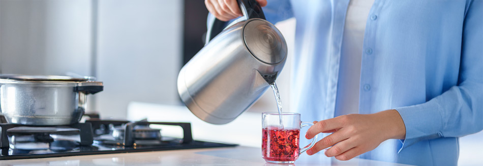 Eine Frau gießt heißes Wasser in eine Tasse und brüht sich so einen Tee.