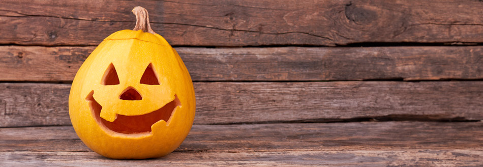 Ein Kürbis mit einem fröhlichen Schnitzgesicht lächelt auf einer Holzfläche in den Tag hinein.