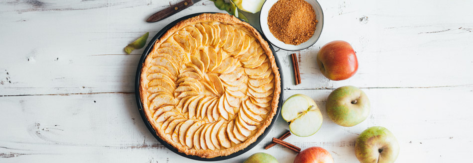 Welche Äpfel für Apfelkuchen? Ein gebackener Kuchen steht neben einigen Äpfeln und Zimt