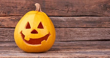 Ein Kürbis mit einem fröhlichen Schnitzgesicht lächelt auf einer Holzfläche in den Tag hinein.