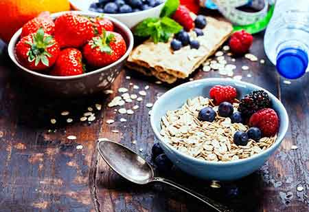 Eine Schale mit Müsli und Beeren steht neben einer Schale mit Erdbeeren