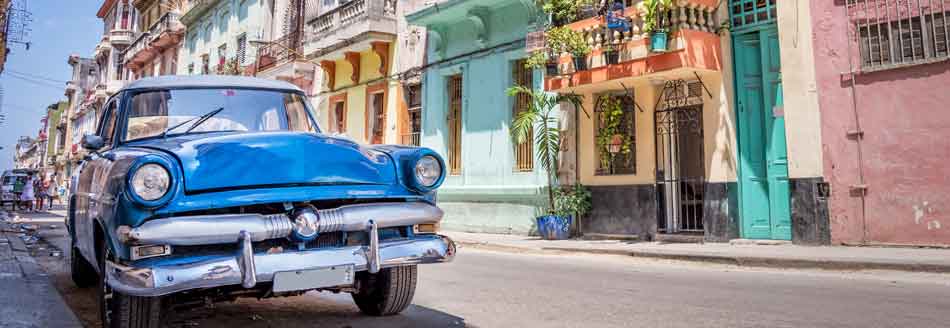 Ein Oldtimer steht vor kunterbunten Häusern in Kuba