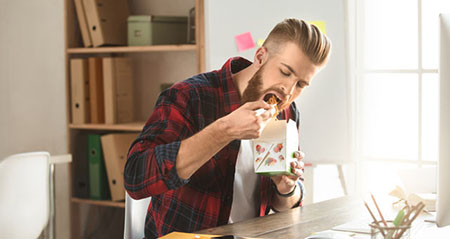 Schnell essen macht dick: Ein Mann isst am Arbeitsplatz